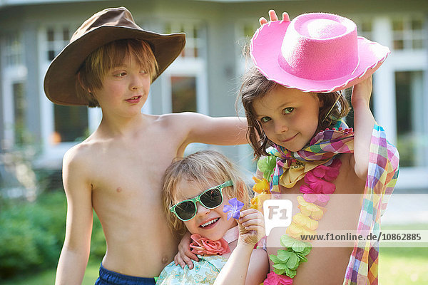 Porträt von Mädchen und Jungen mit Cowboyhut und Sonnenbrille im Garten