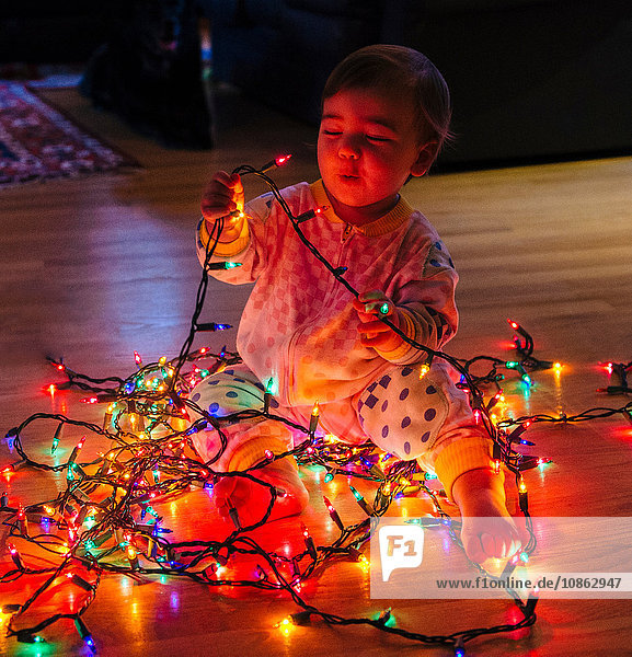 Female toddler playing with multi-coloured christmas lights on floor