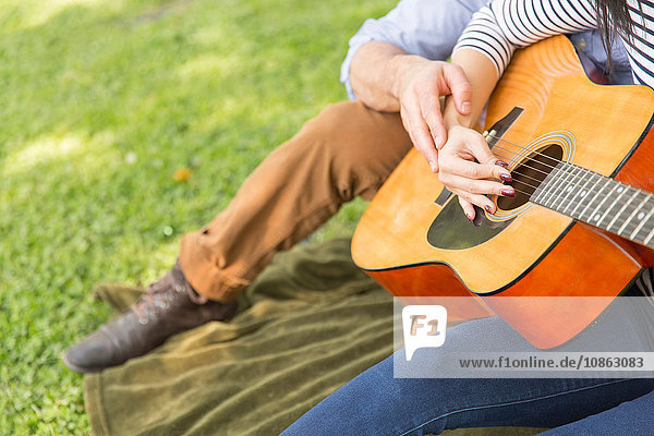 Ausschnitt eines Paares,  das auf Gras sitzt und akustische Gitarre spielt