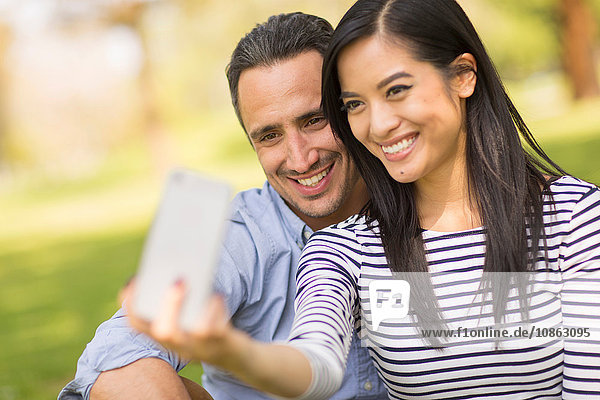 Couple sitting on grass using smartphone to take selfie