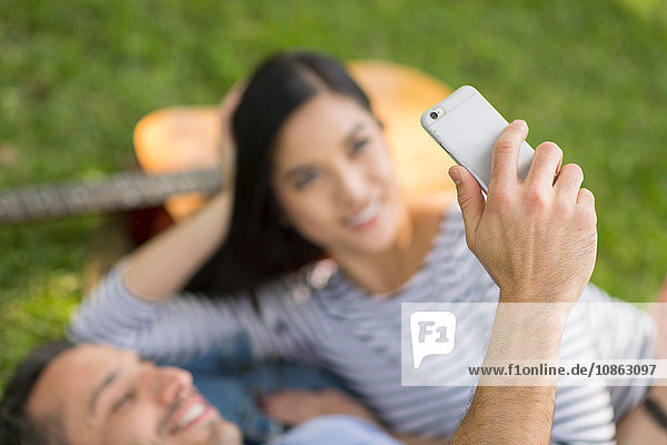 Paar  das auf dem Rasen liegt und sein Smartphone benutzt  um Selfie zu nehmen