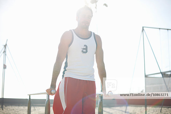 Mittelgroßer erwachsener Mann  der am Strand trainiert und dabei parallele Gymnastikbalken benutzt