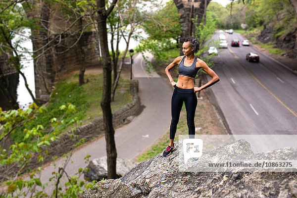 Frau in Sportkleidung steht auf Felsen über der Autobahn