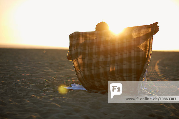 Couple on beach at sunset man putting blanket around them