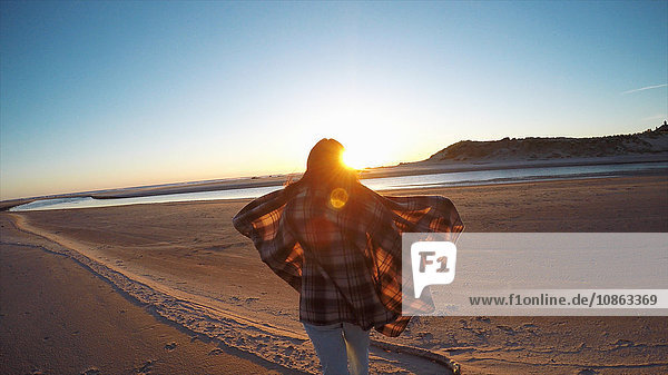 Rückansicht einer Frau mit wehendem Schal  die den Sonnenuntergang von Cannon Beach  Oregon  USA  aus beobachtet
