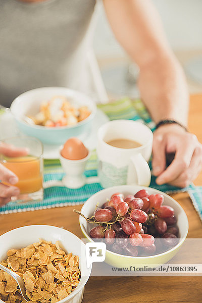 Schnappschuss eines jungen Mannes am Frühstückstisch mit Müsli  gekochtem Ei und Weintrauben