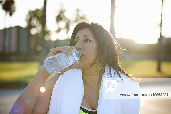 Frau mit Handtuch auf den Schultern trinkt Wasser aus Plastikflasche