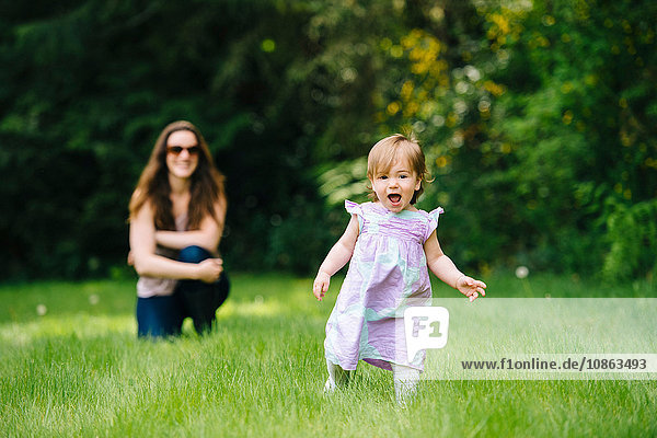 Weibliches Kleinkind rennt vor der beobachtenden Mutter im Park weg
