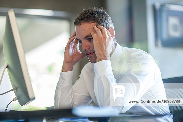 Stressed businessman with hands on forehead at office desk
