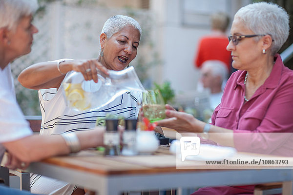Ältere Frau und Freunde gießen Wasser im städtischen Straßencafé