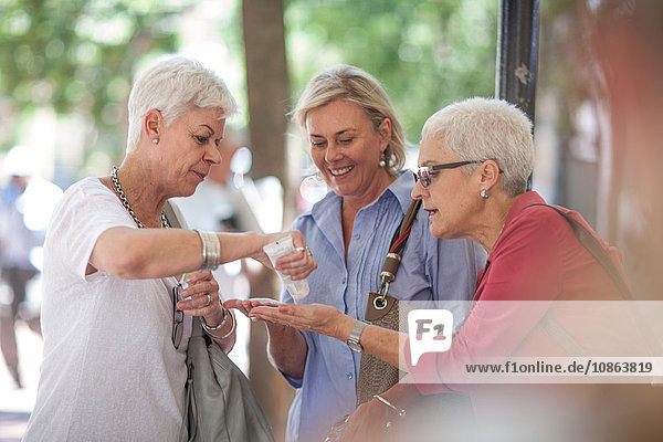 Senior and mature women sharing hand cream in city