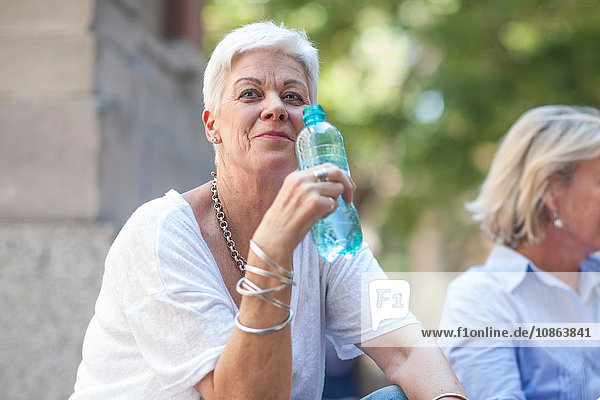 Ältere Frau sitzt mit einer Flasche Wasser in der Stadt