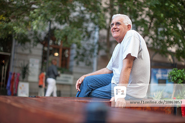 Älterer Mann sitzt in der Stadt auf der Mauer
