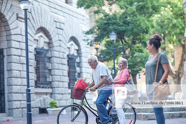Junge Frau beobachtet älteren Mann und Frau beim gemeinsamen Radfahren in der Stadt