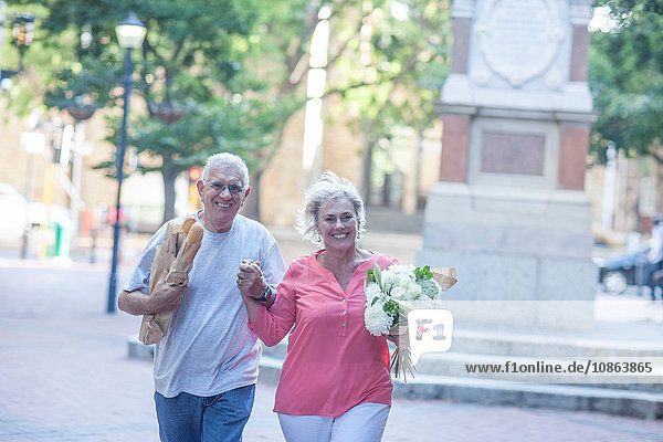 Porträt eines glücklichen älteren Ehepaares mit Baguette und Blumenstrauss in der Stadt