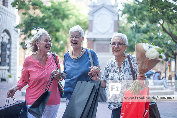 Glückliche ältere und reifere Frauen  die in der Stadt Einkäufe und Blumensträuße tragen