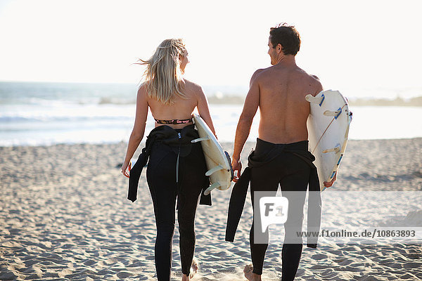 Rear view of surfing couple carrying surfboards on Venice Beach  California  USA