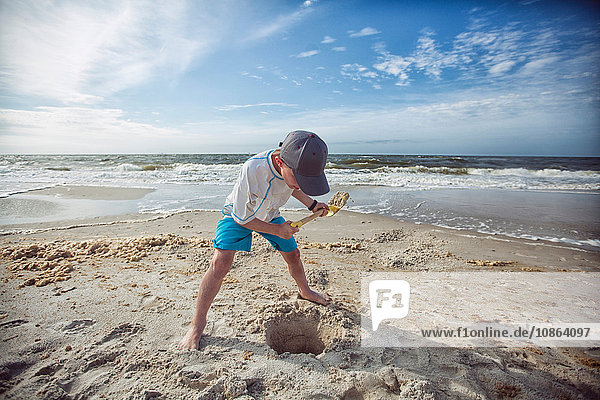 Junge am Strand gräbt Loch im Sand