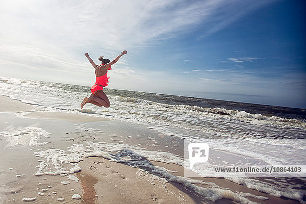 Seitenansicht eines Mädchens am Strand mit erhobenen Armen,  das in die Luft springt