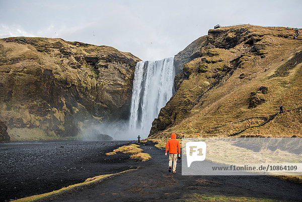 Rückansicht von Menschen  die auf vulkanischer Landschaft zum Wasserfall gehen  Skogafoss  Island