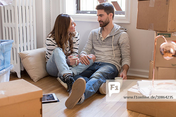 Moving house: Young couple sitting in room full of boxes  drinking hot drink