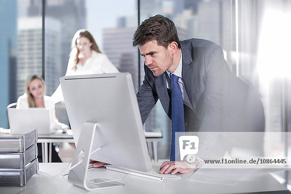 Geschäftsmann mit Computer im Büro  Kollegen arbeiten im Hintergrund
