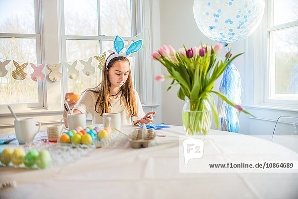 Teenager-Mädchen liest Texte  während sie hart gekochte Eier für Ostern bei Tisch färbt