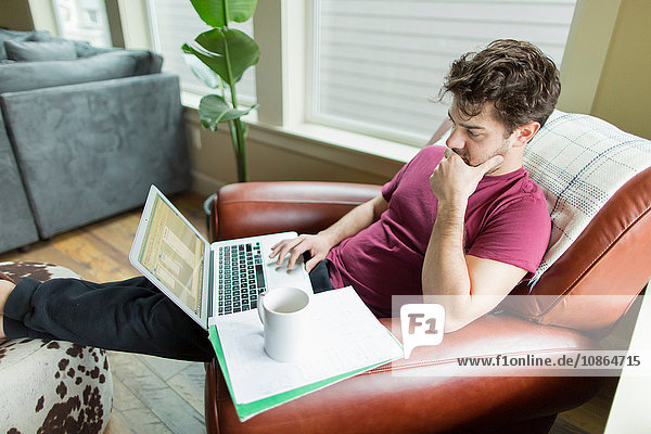 Man on living room armchair with feet up working on laptop