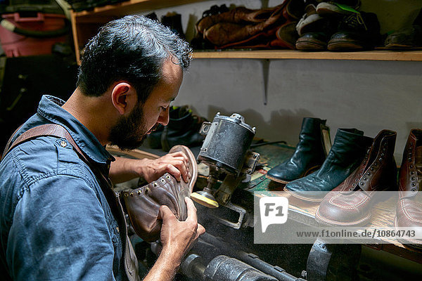 Male cobbler in traditional shoe workshop inspecting boot
