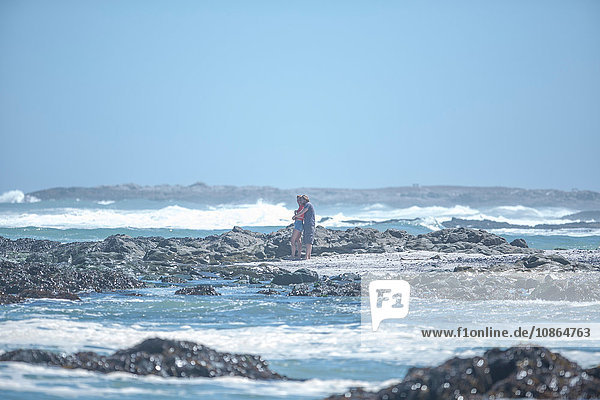 Distanzansicht eines jungen Paares  das sich am Strand umarmt  Kapstadt  Südafrika