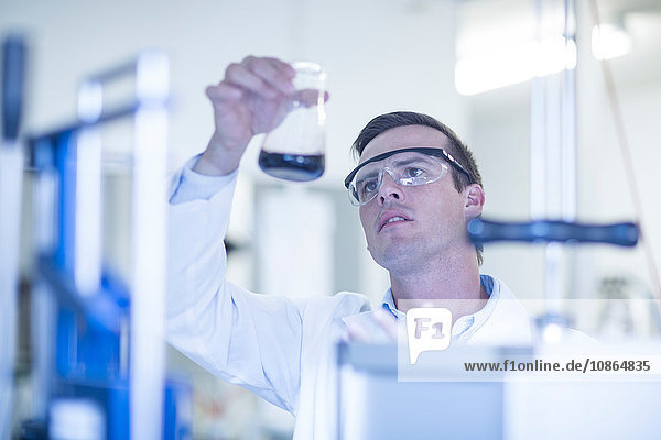 Mittelgroßer erwachsener Mann im Labor  betrachtet Flüssigkeit in Glaskolben