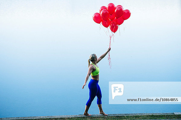 Side view of woman holding bunch of red balloons