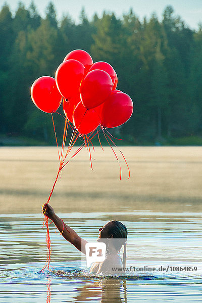 Woman in water holding bunch of red balloons