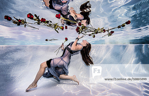 Frau trägt Kleid unter Wasser im Schwimmbad mit Rosen
