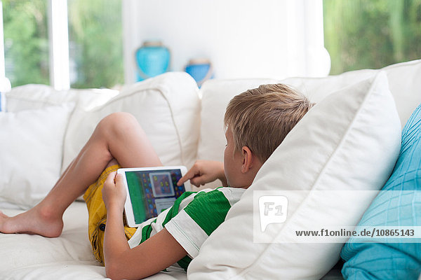 Auf dem Sofa liegender Junge mit digitalem Tablett