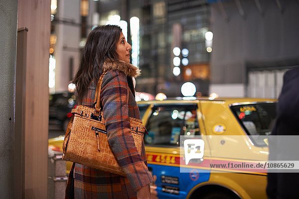 Seitenansicht einer reifen Frau  die eine Handtasche auf der Schulter trägt und darauf wartet  die Straße zu überqueren  Ginza  Tokio  Japan