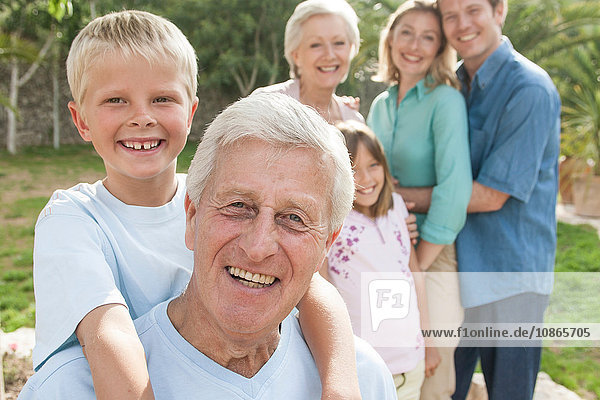 Porträt eines älteren Mannes und seines Enkels vor der Familie,  die lächelnd in die Kamera blicken
