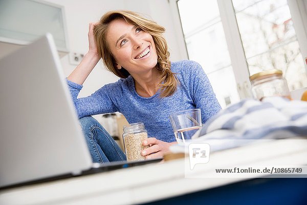 Happy woman sitting at kitchen table with laptop