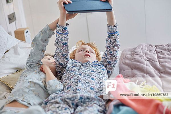 Kinder im Schlafanzug mit digitalem Tablett im Bett