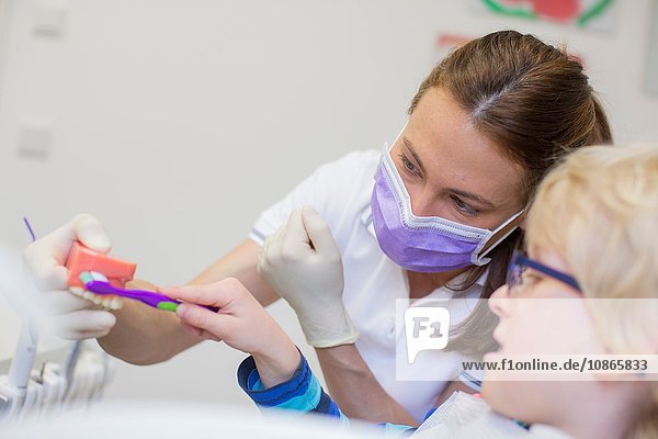 Junge und Zahnarzt in Zahnarztpraxis beim Bürsten von Zahnersatz