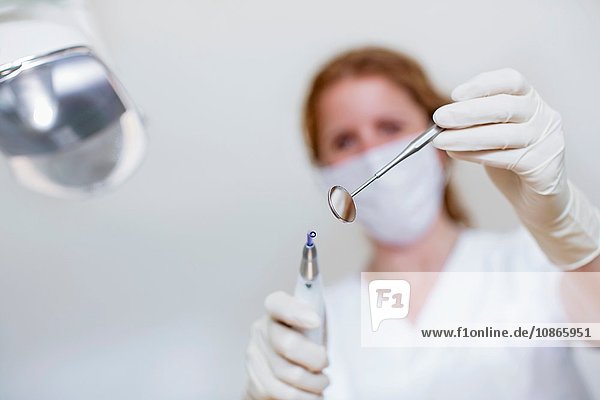Niedrigwinkelansicht eines Zahnarztes  der eine Maske und Schutzhandschuhe trägt und eine zahnärztliche Ausrüstung und einen Zahnarztspiegel hält