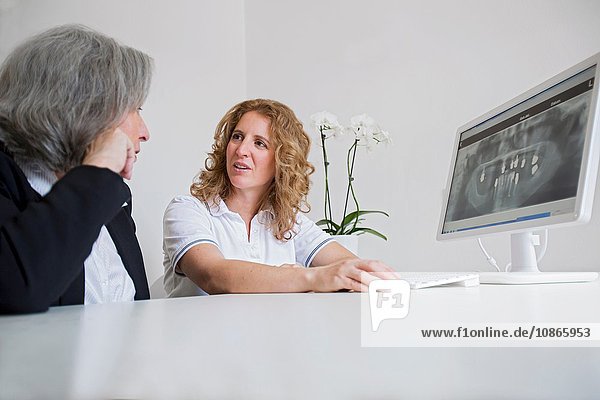Oberflächenansicht einer reifen Frau und einer älteren Frau  die über ein Röntgenbild auf einem Computerbildschirm diskutieren