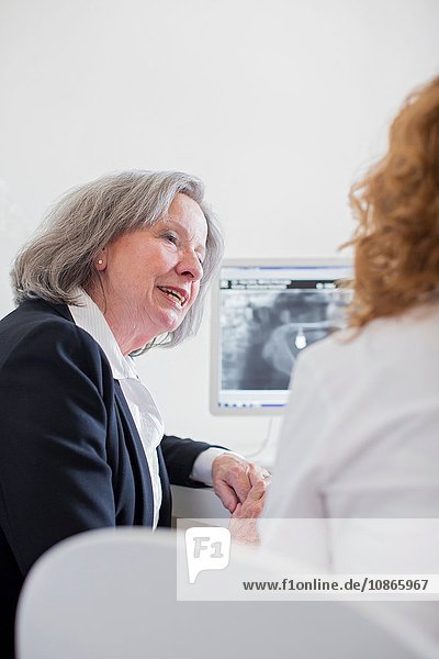 Ältere Frau bespricht Röntgenbild am Computerbildschirm