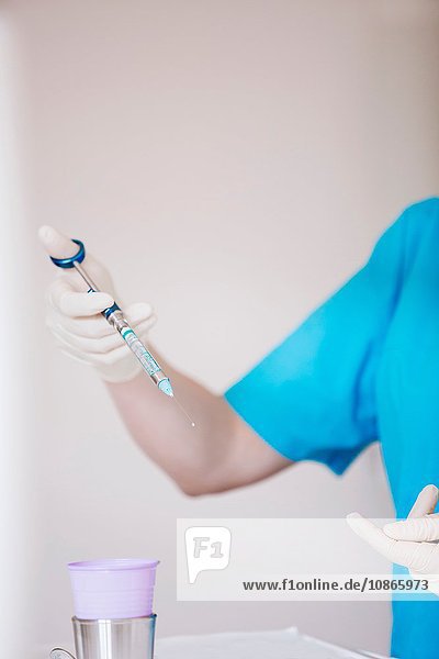 Hände der Zahnarzthelferin mit Schutzhandschuhen  die die Spritze halten