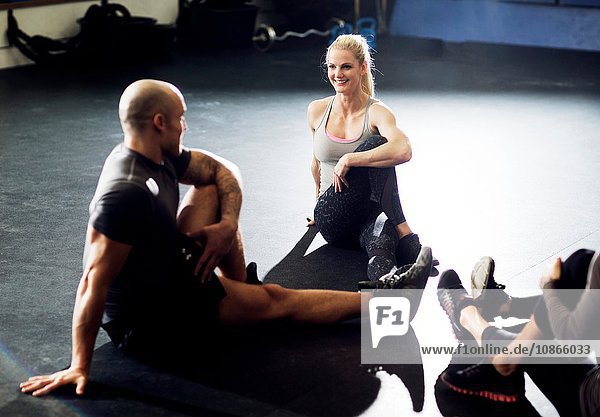Male and female crossfitters sitting in circle doing stretch training