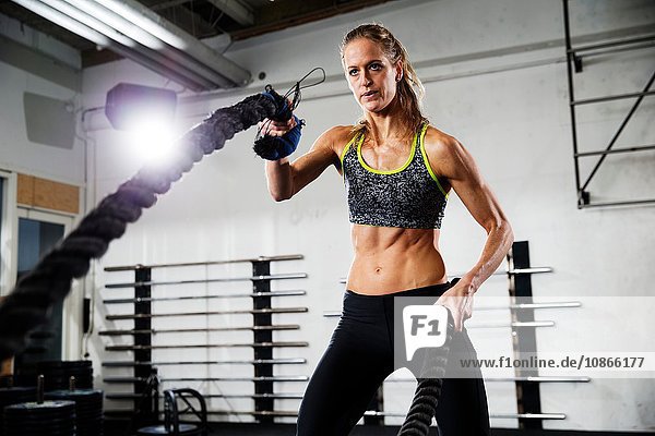 Female crossfitter training with battling rope in gym