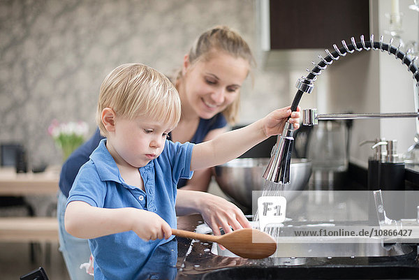 Mother helping son wash wooden spoon