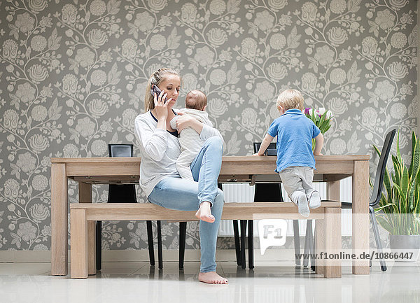 Mutter benutzt Smartphone  während sie den kleinen Jungen hält  der ältere Sohn sitzt neben ihr