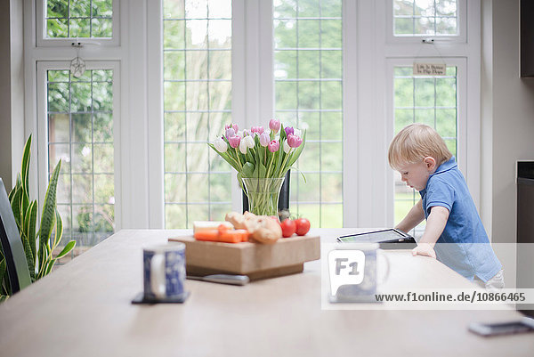 Junge steht am Tisch und schaut auf digitales Tablett