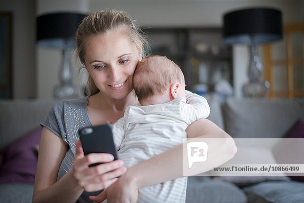 Mutter hält Baby Boy während sie ein Smartphone benutzt